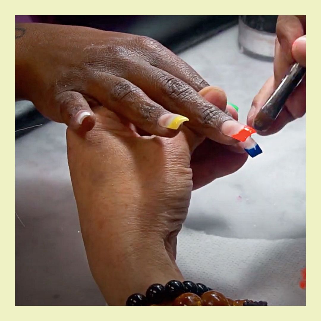 one dark brown hand holds another dark brown hand as nails are being painted